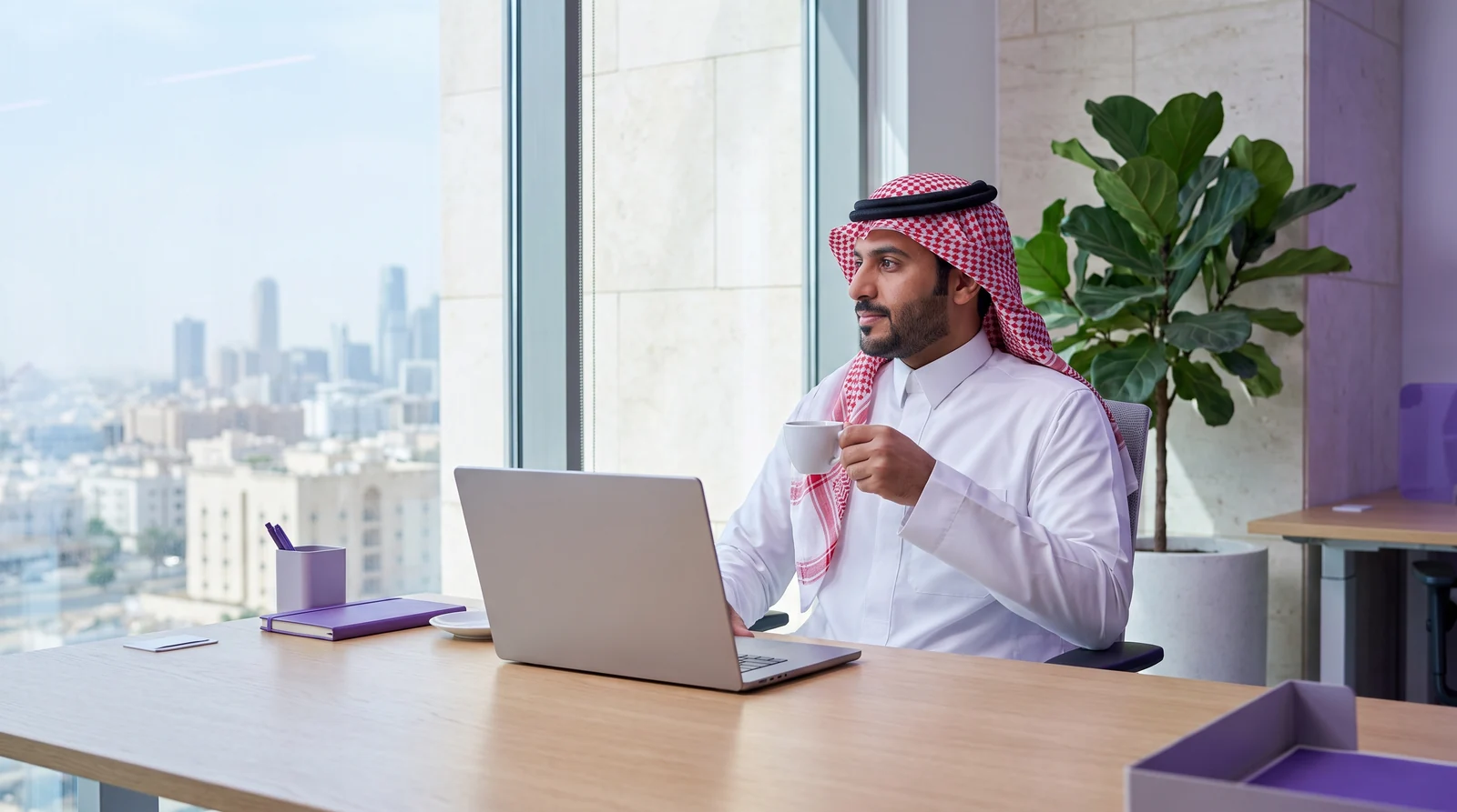 A professional holding a cup while working at a laptop